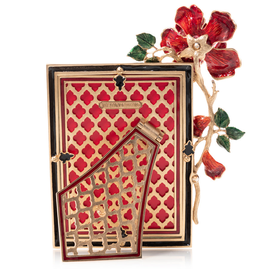 5" x 7" - Red Rose - Picture Frame The back of this exquisite Jay Strongwater picture frame features a striking gold-tone lattice design with repeating ruby-red, four-petal shapes, surrounded by glossy black enamel trim. A beautifully sculpted golden branch extends along the right side, adorned with a large, deep red flower, delicate buds, and glossy green leaves. The hinged gold easel stand showcases intricate, lace-like floral openwork with coordinating burgundy enamel edging.