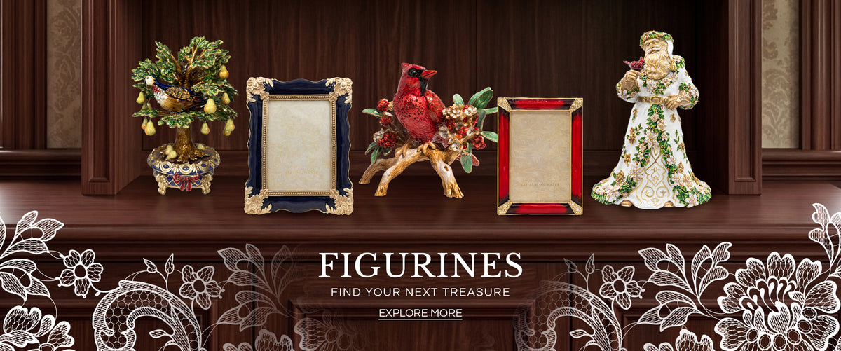 Promotional banner for "FIGURINES - FIND YOUR NEXT TREASURE" featuring Jay Strongwater decor pieces arranged on a dark wood mantle: a jeweled partridge pear tree figurine, a dark blue enamel photo frame with ornate gold trim, a red cardinal perched on a leafy branch figurine, a red crystal picture frame, and an elaborate white-and-gold Santa figurine holding a small bird.